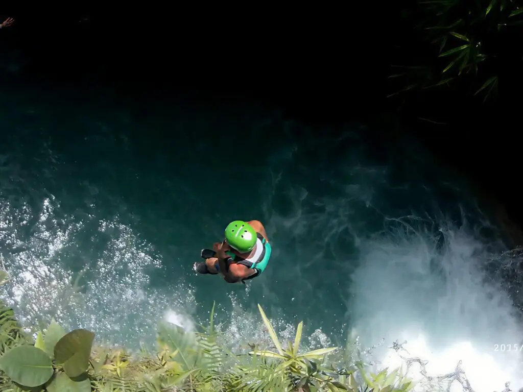 Person in green helmet rappelling down a waterfall.