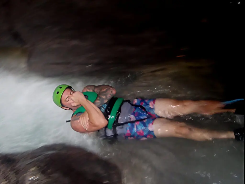 Person floating on water wearing a helmet and life vest in a dark cave.