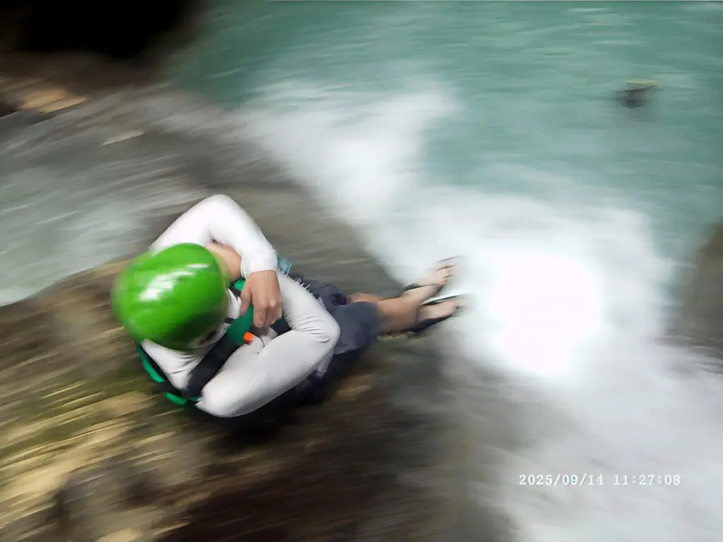 Person wearing a green helmet sliding down a rocky water stream.