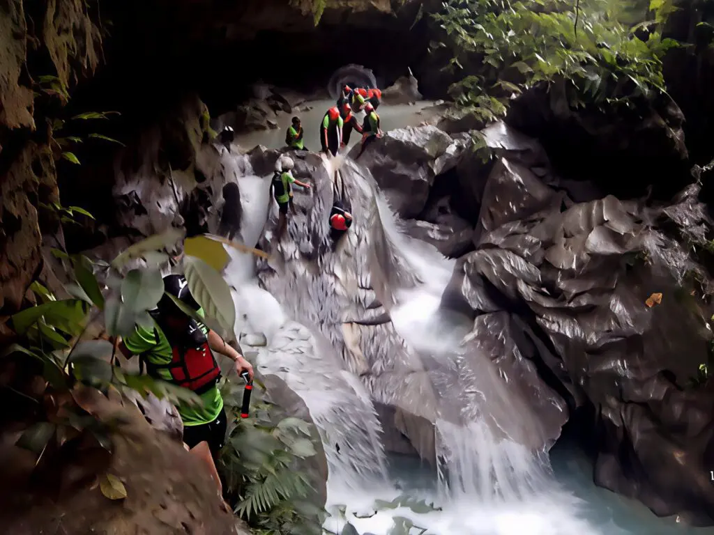 Group of people canyoning down a rocky waterfall.