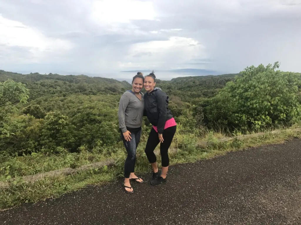 Two women posing on a scenic road with lush greenery behind them.