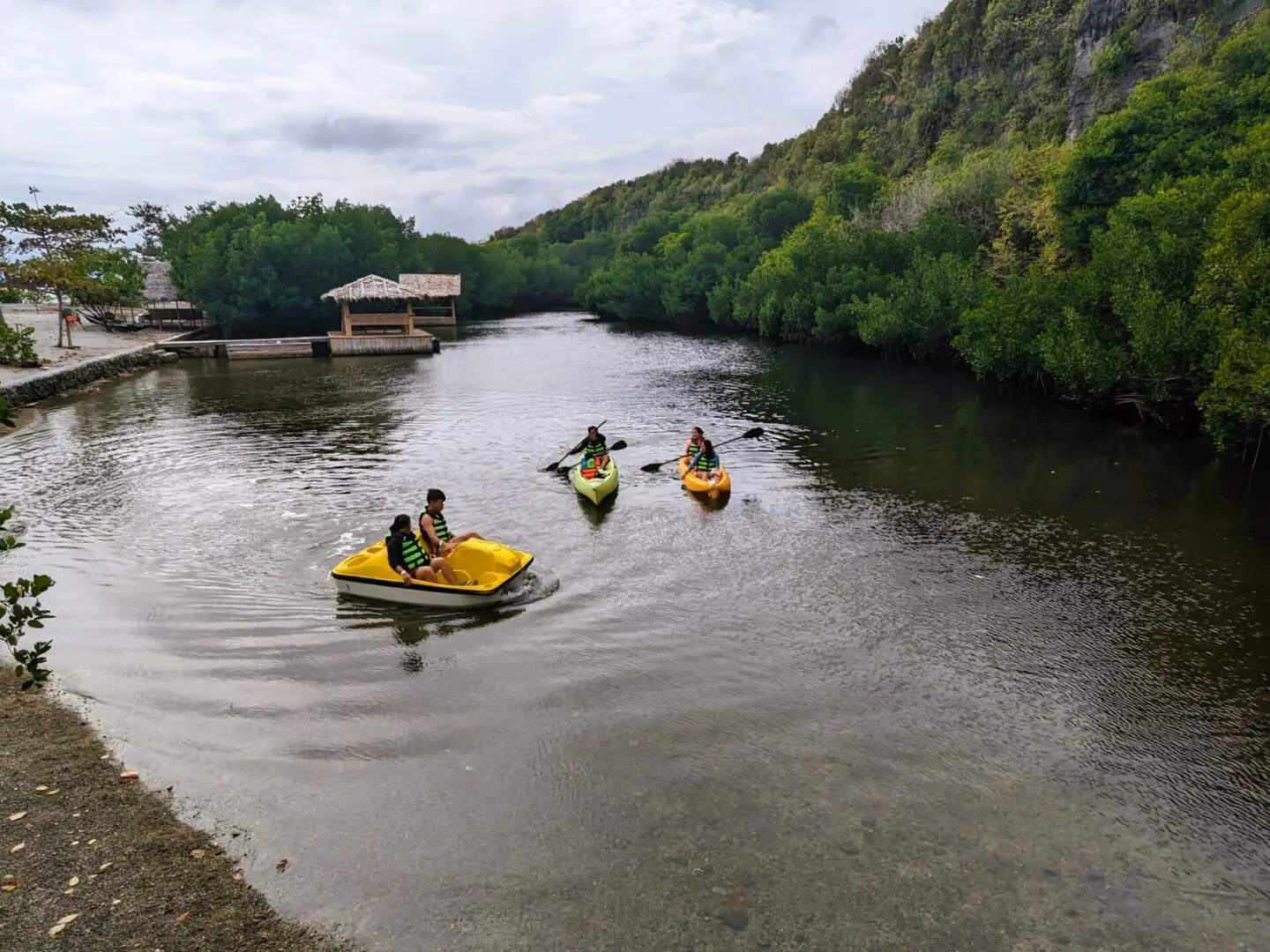 People kayaking on a calm river surrounded by hills.