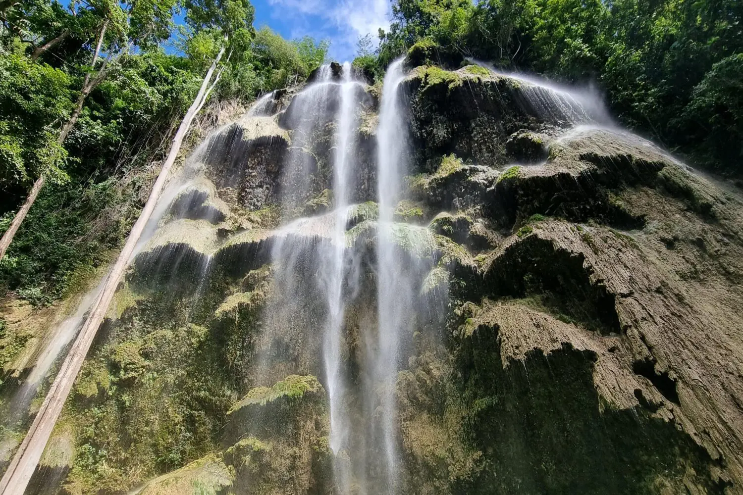A tall waterfall cascading down a rocky cliff surrounded by greenery.