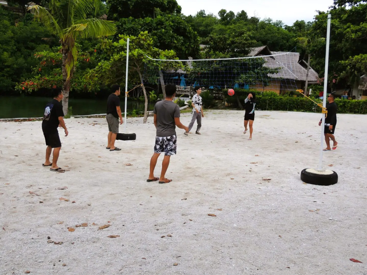 People playing volleyball on a sandy court outdoors.