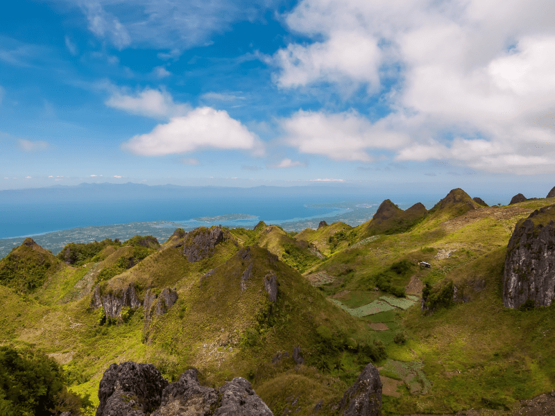 Lush green hills under a partly cloudy blue sky near the coastline.