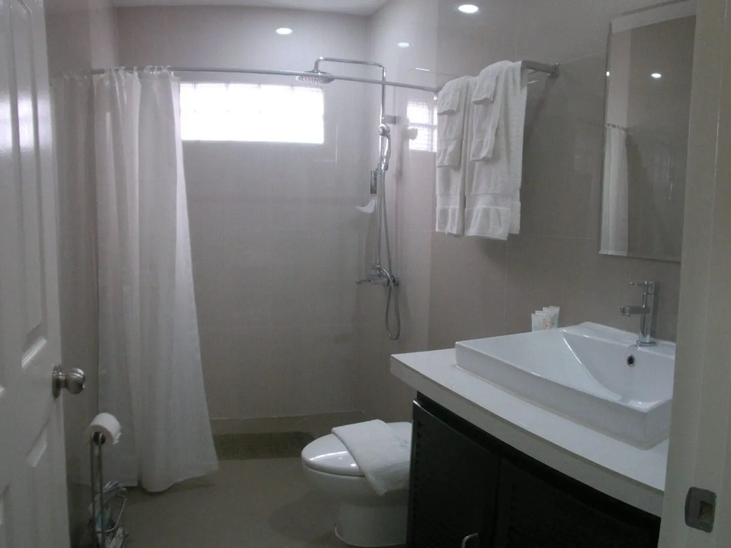 Bright bathroom with white tiles, shower, and sink area.