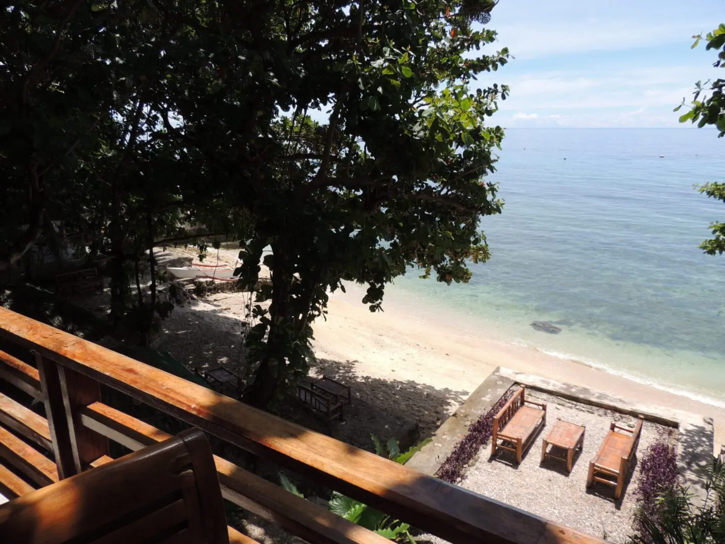 Beach view with lounge chairs and a tree from a wooden balcony.