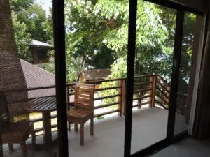A peaceful balcony with wooden chairs overlooking green trees.
