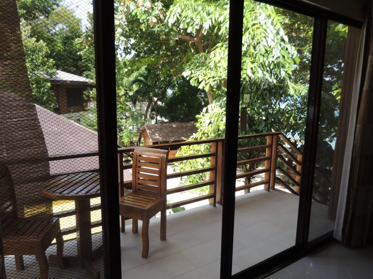 A peaceful balcony with wooden chairs overlooking green trees.