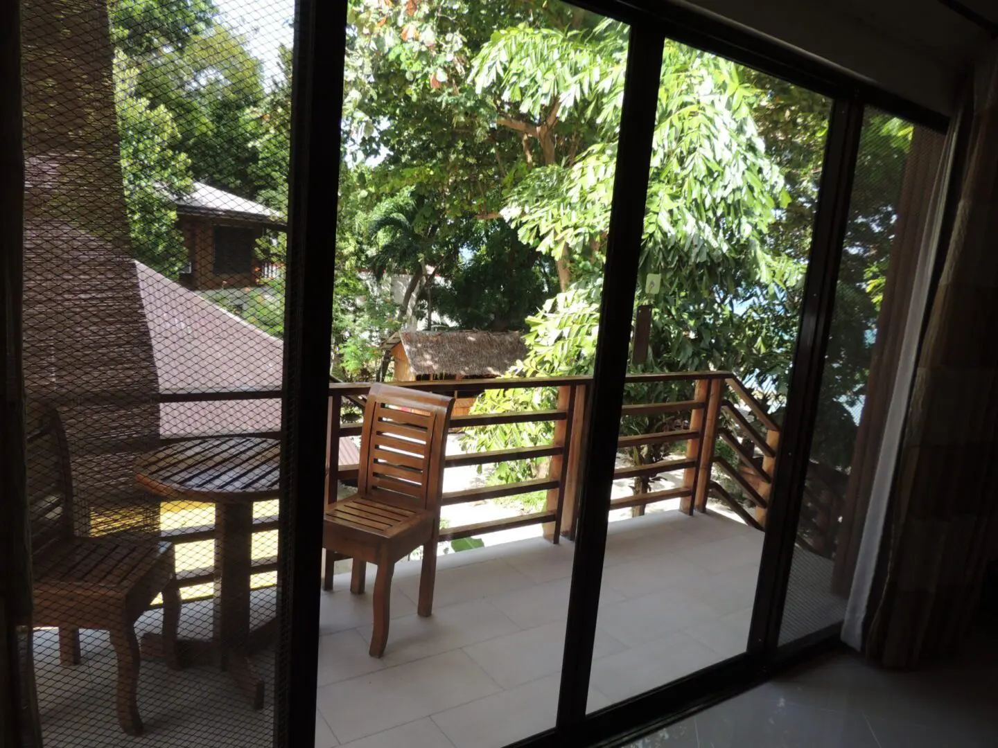 Balcony with wooden chairs overlooking lush greenery through glass doors.