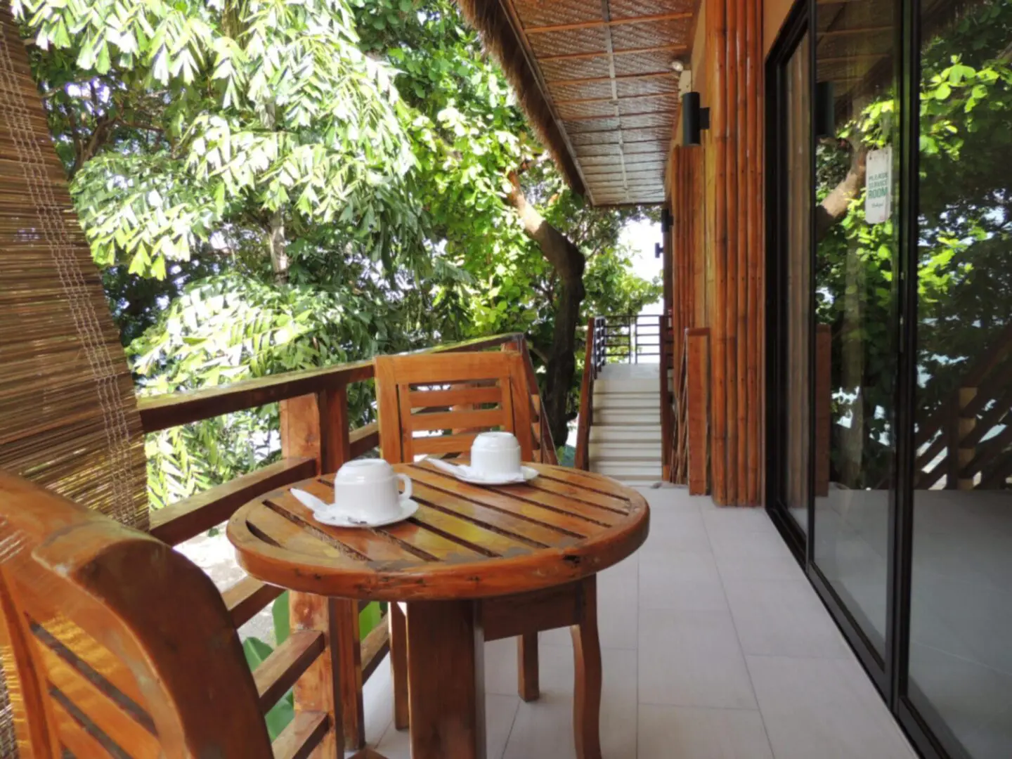 Cozy balcony with wooden table and chairs surrounded by lush greenery.