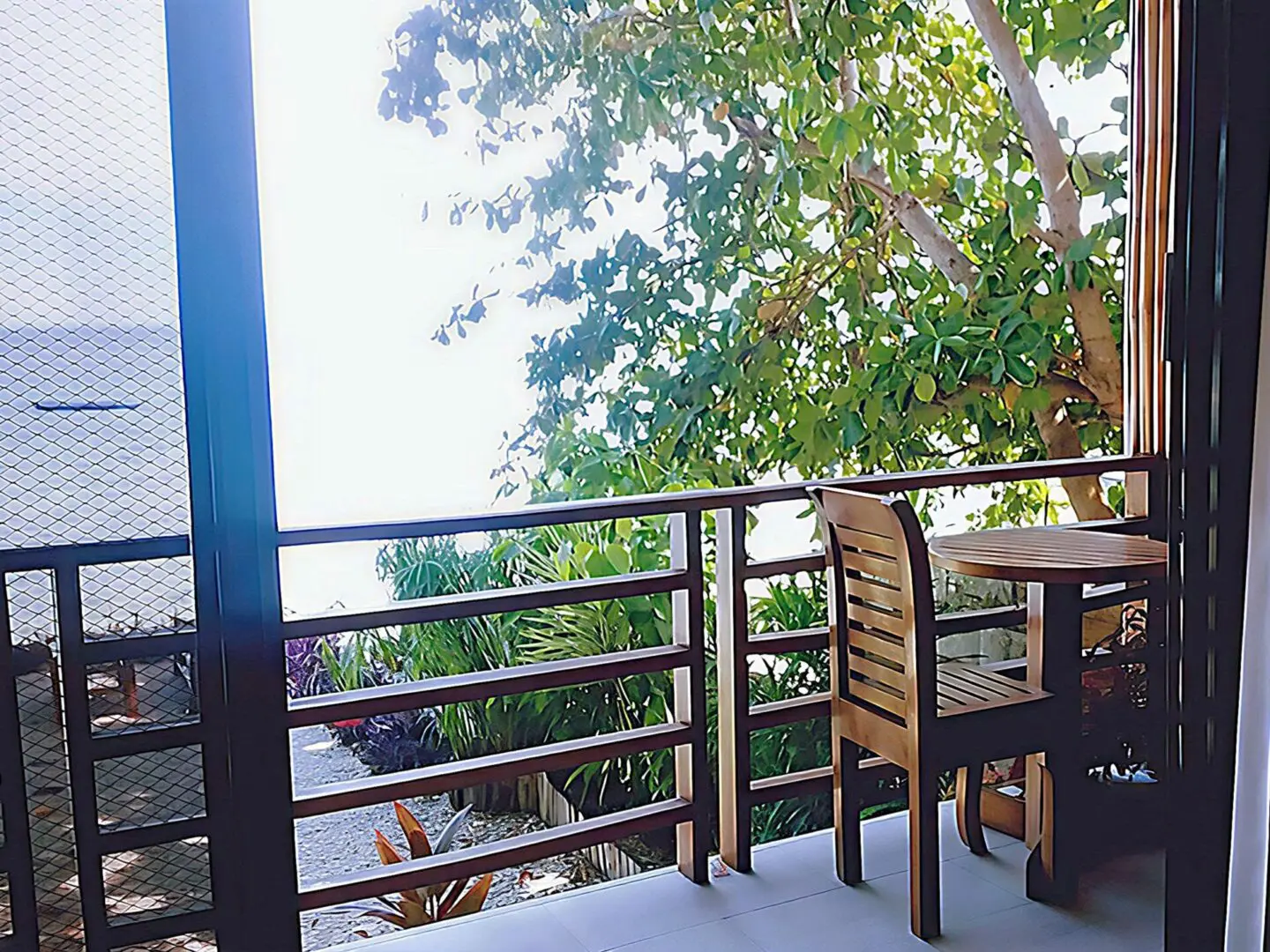 Balcony with a peaceful view of trees and a chair beside a table.